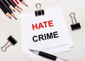On a light background, black pencils, black paper clips, a pen and a sheet of white paper with the text HATE CRIME Royalty Free Stock Photo