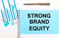 On a light background - light blue diagrams, paper clips and a sheet of paper with the text STRONG BRAND EQUITY. View from above.