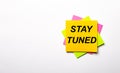 On a light background - bright multicolored stickers with the text STAY TUNED. Copy space