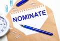 On a light background, a craft envelope, an alarm clock, paper clips, a blue pen and a sheet of paper with the text NOMINATE Royalty Free Stock Photo