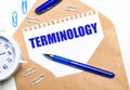 On a light background, a craft envelope, an alarm clock, paper clips, a blue pen and a sheet of paper with the text TERMINOLOGY Royalty Free Stock Photo