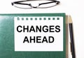 On a light background, glasses, a pen, a green notebook and a white sheet of paper with the text CHANGES AHEAD Royalty Free Stock Photo