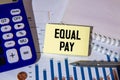 notebook and a white sheet of paper with the text EQUAL PAY. Royalty Free Stock Photo