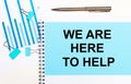 On a light background - light blue diagrams, paper clips and a sheet of paper with the text WE ARE HERE TO HELP. View from above.