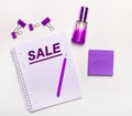 On a light background - a lilac gift, perfume, lilac business accessories and a notebook with a lilac inscription SALE. Flat lay.