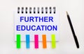 On a light background, a pen, a notebook with the text FURTHER EDUCATION and bright stickers