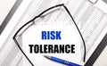 On a light background, a report, black-framed glasses, a pen and a sheet of paper with the text RISK TOLERANCE. Business concept