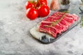 On a light background, sliced raw meat steaks on a cutting board with a sprig of rosemary, ripe tomatoes, spices, seasonings in Royalty Free Stock Photo