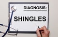 On a light background, a stethoscope and a sheet of paper, on which a man writes SHINGLES. Medical concept