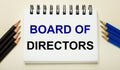 On a light background, a white notebook with the text BOARD OF DIRECTORS and black and blue pencils on the sides Royalty Free Stock Photo