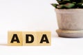 On a light background, wooden cubes with the inscription ADA Americans with Disabilities Act and a flower in a pot. Defocus Royalty Free Stock Photo