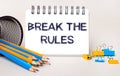 On a light background, yellow and blue pencils and paper clips and a white notebook with the text BREAK THE RULES Royalty Free Stock Photo