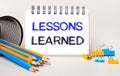 On a light background, yellow and blue pencils and paper clips and a white notebook with the text LESSONS LEARNED Royalty Free Stock Photo