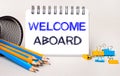 On a light background, yellow and blue pencils and paper clips and a white notebook with the text WELCOME ABROAD Royalty Free Stock Photo