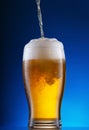 Light beer pouring into glass on blue background Royalty Free Stock Photo