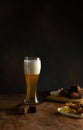 Light beer in a tall glass, beer snacks, grilled meat on a wooden table on a dark background, close-up Royalty Free Stock Photo