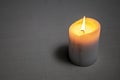 Light beige candle burning with a bright yellow flame. Wax flows down to the table. A small shadow falls on the light table from Royalty Free Stock Photo