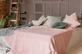 Light beige pink blanket on bed with green mint pillows. Stylish cozy scandinavian bedroom interior: bed, wooden ladder