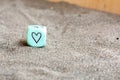 Light blu plastic cube with heart and weather symbols on it's sides. Funny gambling dice on sand. Saint Valentines