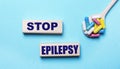 On a light blue background, bright multi-colored pills in a spoon and two wooden blocks with the text STOP EPILEPSY. Medical