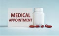 On a light blue background a card  with the text MEDICAL APPOINTMENT near the white bottle pills Royalty Free Stock Photo