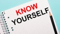 On a light blue background, a checkered notebook with the words KNOW YOURSELF and a black pencil Royalty Free Stock Photo