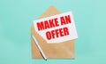 On a light blue background lies an open craft envelope, a white pen and a white sheet of paper with the text MAKE AN OFFER Royalty Free Stock Photo