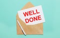 On a light blue background lies an open craft envelope, a white pen and a white sheet of paper with the text WELL DONE Royalty Free Stock Photo