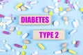 On a light blue background, multi-colored pills and wooden blocks with the text DIABETES TYPE 2. Pharmaceutics. Medical concept