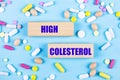 On a light blue background, multi-colored pills and wooden blocks with the text HIGH COLESTEROL. Pharmaceutics. Medical concept Royalty Free Stock Photo