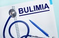 On a light blue background, an open notebook with the word BULIMIA, a blue pen and a stethoscope. View from above. Medical concept Royalty Free Stock Photo