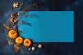 Light blue blank rectangular sheet and pumpkins, leaves, twig on dark blue textured background.