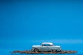 Light blue car figurine placed on top of a heap of golden coins, on blue background