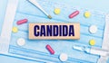 On a light blue disposable face mask there are tablets, a thermometer, an ampoule and a wooden block with the text CANDIDA.
