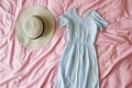 light blue dress next to a sunhat on pink sheets