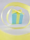 Light blue Gift box at the end of the spiral yellow ribbon, grey background, vertical. Royalty Free Stock Photo