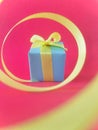 Light blue gift box at the end of the spiral yellow ribbon, red background. Vertical. Royalty Free Stock Photo