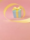 Light blue gift box at the end of the spiral yellow ribbon, pink background, Vertical. Royalty Free Stock Photo