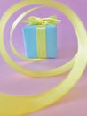 Light blue Gift box at the end of the spiral yellow ribbon, purple background, vertical. Royalty Free Stock Photo