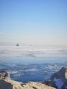 Rocky outcrop in front of boats and sheets of ice in ocean.