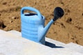 Light blue plastic watering can with black top left on unfinished new concrete steps surrounded with dry soil