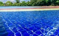 Light blue, red, yellow and blue striped mosaic floor of fountain covered with clear water on the background of blury trees