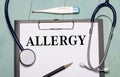 On a light blue wooden background, there is a paper labeled ALLERGY, a stethoscope, an electronic thermometer, and a pen. Medical
