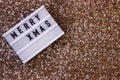 Light board inscription Merry Xmas on a gold sequin background. Winter holiday Royalty Free Stock Photo