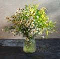 Light bouquet of wildflowers with the prevalence of daisies in a glass vase on a dark table