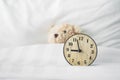 light brown analog clock on white bed with blurred brown bear doll in bedroom Royalty Free Stock Photo