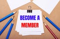 On a light brown background, blue and red pencils and white paper with the text BECOME A MEMBER