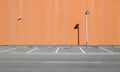 Light brown concrete wall with a lamppost and a surveillance camera. Sidewalk and asphalt road with parking in front.