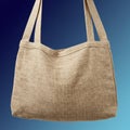A light brown, rectangular jute bag is suspended against a gradient blue background. Royalty Free Stock Photo