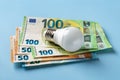 Light bulb on 50 and 100 euro currency banknotes over blue background. High energy costs concept. Power price rising in Europe. Royalty Free Stock Photo